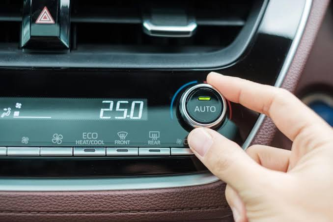 Hand adjusting car climate control dial set to AUTO at 25°C